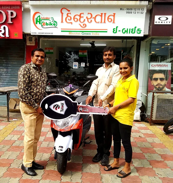 A customer receiving an oversized ceremonial key for a new orange and white electric scooter