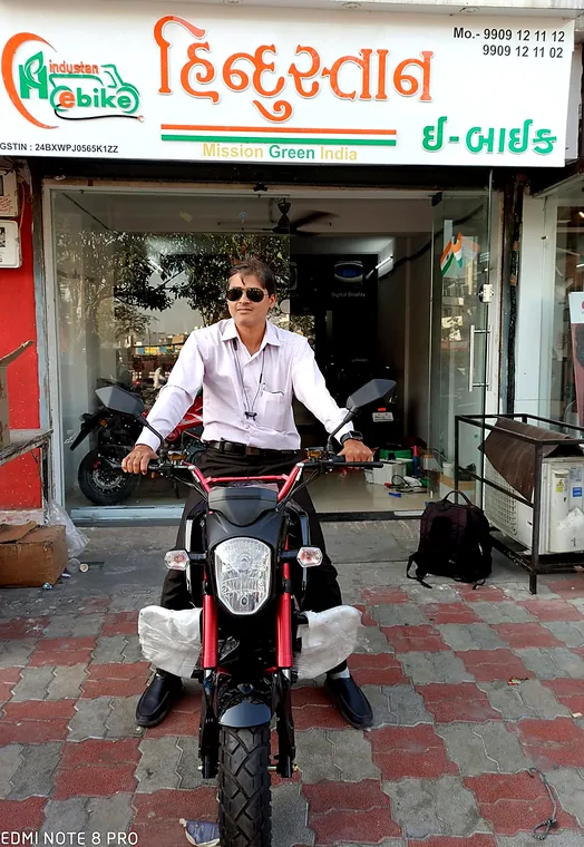 A rider seated on a red and black Tunwal electric motorcycle outside the showroom