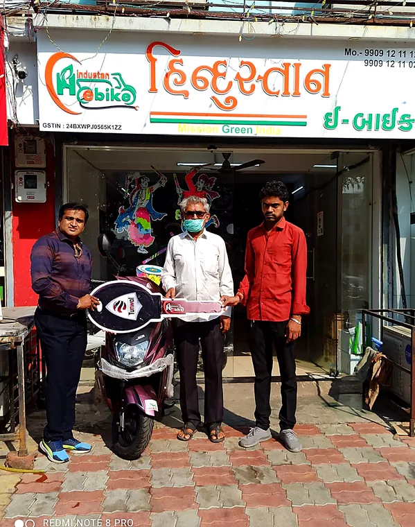 Three people with a maroon electric scooter on delivery day outside the showroom
